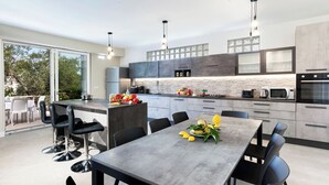 A modern kitchen with a central island, built-in appliances, and a dining area with a table and chairs. - Villa Priora near Sorrento (Priora)