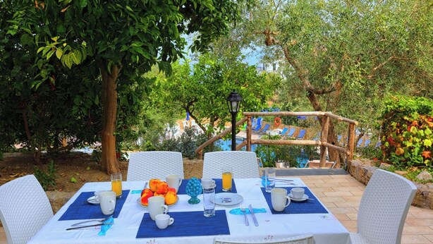 An outdoor dining area with a table set for two, surrounded by lush greenery and a wooden bridge. - Villa Priora near Sorrento (Priora)
