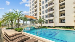A swimming pool with lounge chairs, palm trees, and a building with balconies.