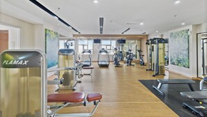 A modern gym with various exercise equipment, including a PLAMAX machine, treadmills, and weight machines.