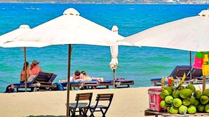 Een strand met parasols, ligbedden en een tafel met kokosnoten.