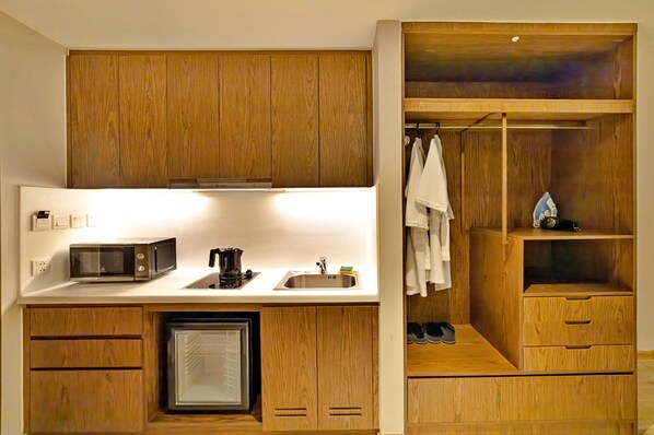 A compact kitchen with a microwave, coffee maker, and sink. There is a small refrigerator and wooden cabinetry.