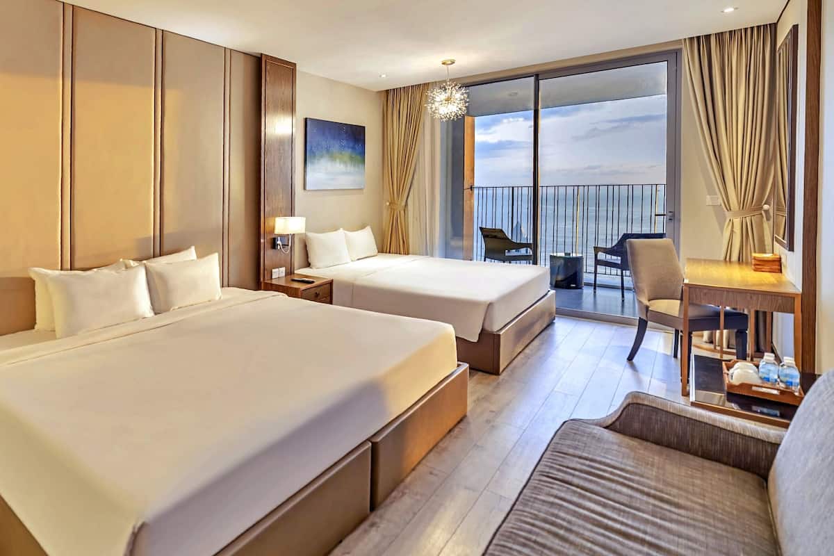 A hotel room with two beds, a desk, a chair, and a balcony with a view.