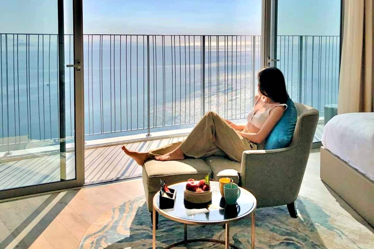A room with a large balcony, a bed, a chair, and a small table with items on it.