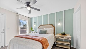 Un dormitorio con cama, mesita de noche, ventilador de techo y ventana.