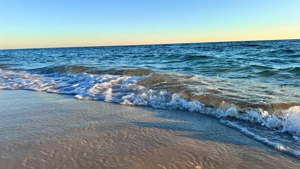 Una playa con olas suaves lamiendo la orilla bajo un cielo despejado.