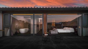 A modern hotel room with a large glass door, a bed, a chair, and a small table with a fruit bowl. - Mangshu Taotangzhiqiu Seaview Hotel (Dali)