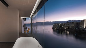 A modern interior with a large glass window overlooking a calm body of water and distant mountains. - Mangshu Taotangzhiqiu Seaview Hotel (Dali)