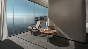 A modern room with a large window overlooking a body of water, a wicker chair, a small round table with a lamp, and a book. - Mangshu Taotangzhiqiu Seaview Hotel (Dali)