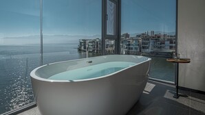 A modern bathroom with a large bathtub, a glass-enclosed window, and a view of a cityscape and mountains. - Mangshu Taotangzhiqiu Seaview Hotel (Dali)