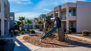 A playground with a slide, surrounded by palm trees and a sandy area, with modern buildings in the background. - GUEST FAVORITE - Pool & Pickleball -Clean & Comfortable-St George Home near Zion (St George)
