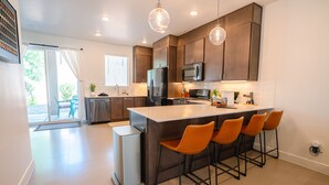 A modern kitchen with dark wooden cabinets, a stainless steel refrigerator, a microwave, and a large island with bar stools. - GUEST FAVORITE - Pool & Pickleball -Clean & Comfortable-St George Home near Zion (St George)