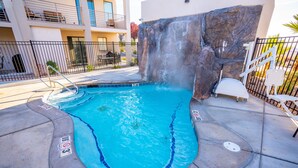 A swimming pool with a waterfall feature, surrounded by a concrete deck and a metal fence. - GUEST FAVORITE - Pool & Pickleball -Clean & Comfortable-St George Home near Zion (St George)