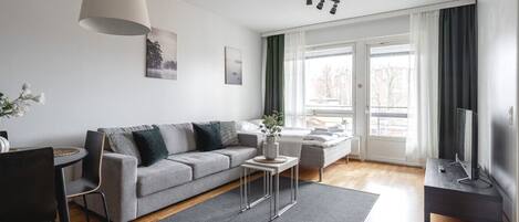 A modern living room with a grey sofa, a coffee table, a TV stand, and a dining area with a table and chairs.