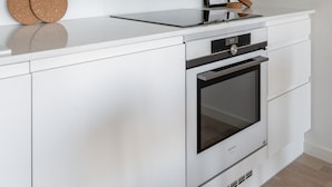A modern kitchen with white cabinetry, a built-in oven, and a countertop with a framed picture and two cork coasters. - Stylish New 1BR Home with Sauna, Hosts 4 Guests (Tampere)