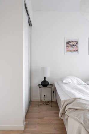 A minimalist bedroom with a single bed, a bedside table with a lamp, and a wall-mounted picture.
