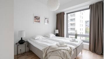 Een moderne slaapkamer met een groot bed, nachtlampjes, uitzicht op gebouwen en kunst aan de muur.