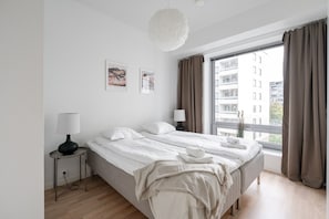 A modern bedroom with a large bed, bedside lamps, a view of buildings, and artwork on the wall.
