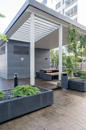 An outdoor seating area with benches and planters, a covered walkway, and a building with a no-smoking sign.