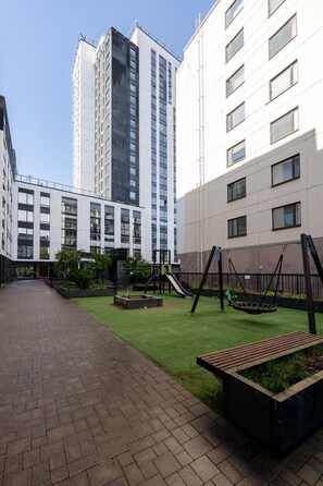 A courtyard with a playground, a brick pathway, and modern buildings in the background.