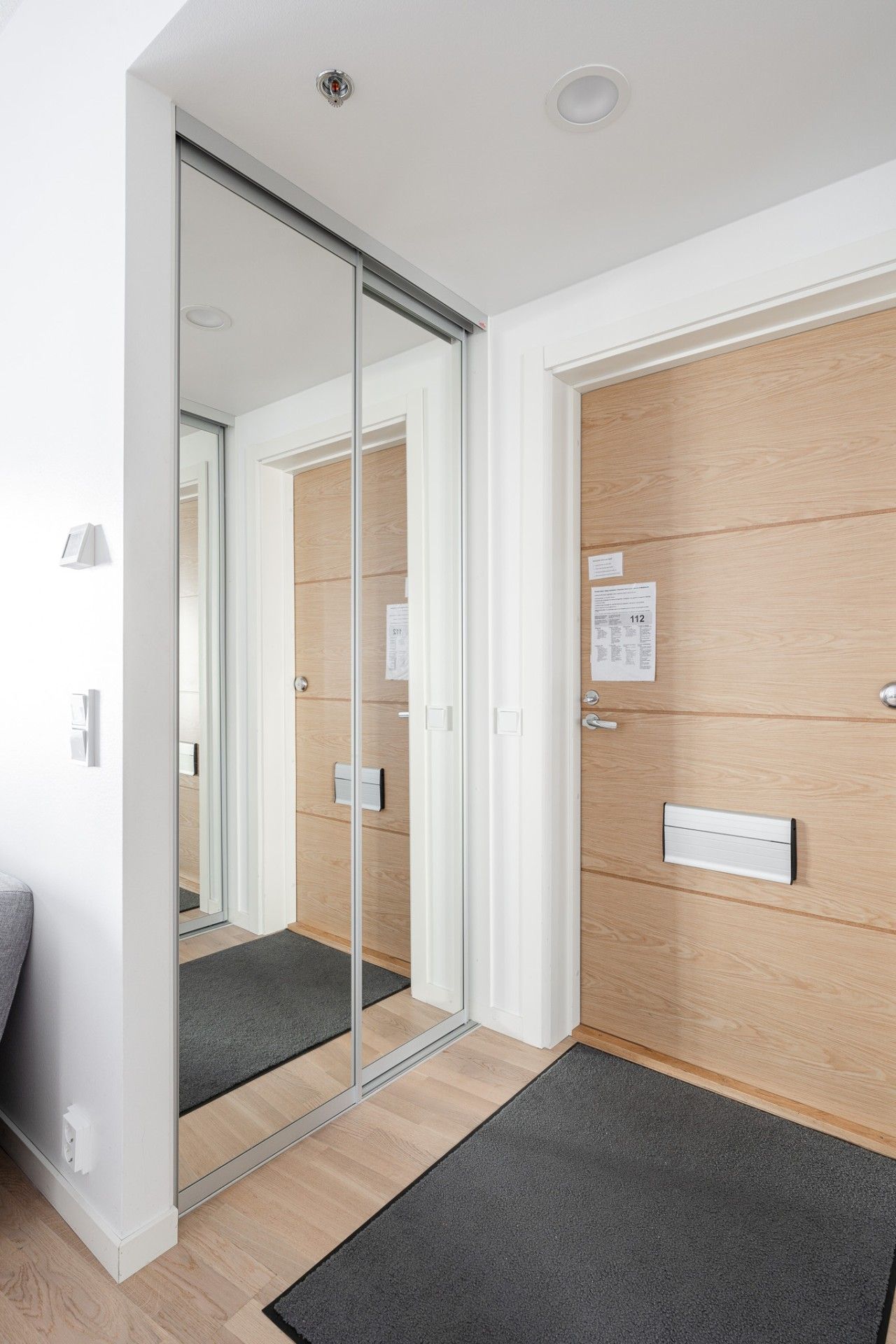 A modern room with a sliding glass door leading to a wooden wall, a small desk with a chair, and a light switch on the wall.
