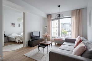 A modern living room with a sofa, a TV, a coffee table, and a bed in the adjacent room.