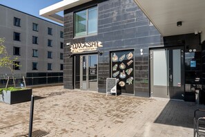 A modern building with a sushi and yakitori grill sign, a glass door entrance, and a paved outdoor area.