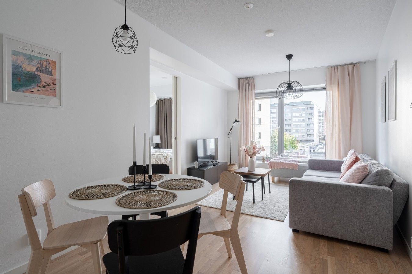 Un salon moderne avec un canapé gris, une table à manger avec des sets de table et une grande fenêtre donnant sur la ville.