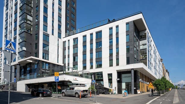 A modern building with a pedestrian overpass, a parking sign, and a storefront labeled "LUMINARY". - Stylish New 1BR Home with Sauna, Hosts 4 Guests (Tampere)
