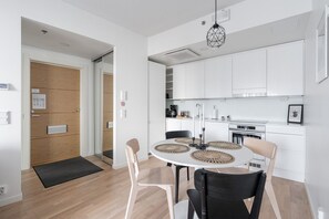A modern kitchen with white cabinets, a dining table with four chairs, and a hanging light fixture.