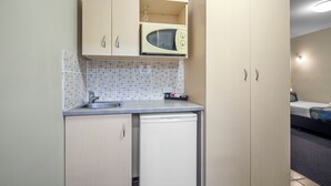 A compact kitchenette with a microwave, sink, and a small refrigerator. - Queen Deluxe Retreat, Smart TV, Kitchenette & More! (Coffs Harbour)