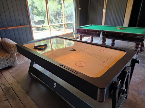 A pool table in a room with a glass-top table, wooden flooring, and a view of greenery outside. - Kangaroo Lake Backpacker C & C Park (Stawell)