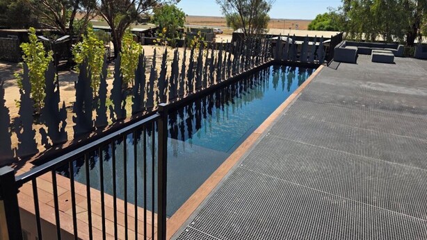 Ein Schwimmbecken mit schwarzem Metallzaun, umgeben von Bäumen und blauem Himmel.