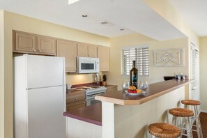 A kitchen with a refrigerator, microwave, stove, and bar stools. - Refined Lake-Access Condo with Screened Porch, Community Pool & Free Tickets! (Kimberling City)