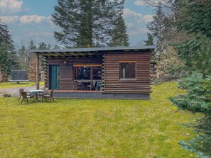 Situated in a wooded environment, this cabin features a cozy porch with a table and chairs for outdoor dining or relaxation.