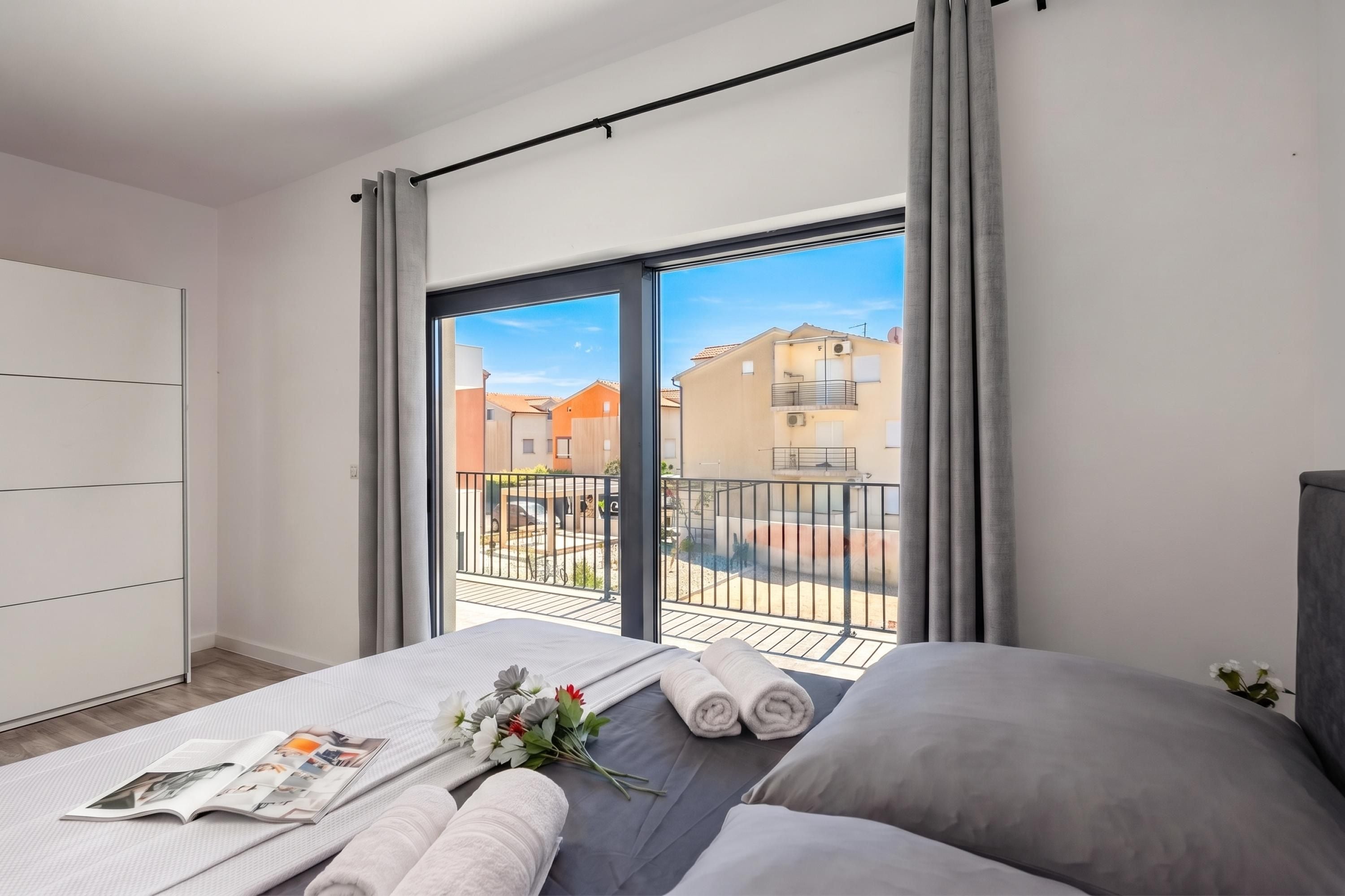 A modern bedroom with a large bed, a view of a courtyard, and a balcony with a railing.