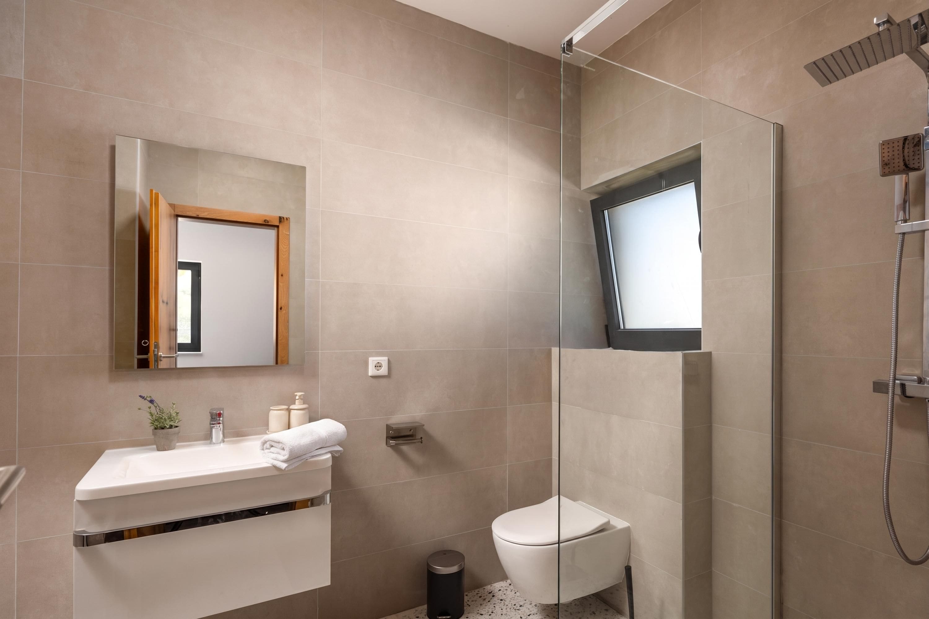 Et moderne badeværelse med brusekabine i glas, et hvidt toilet og en vask med spejl.