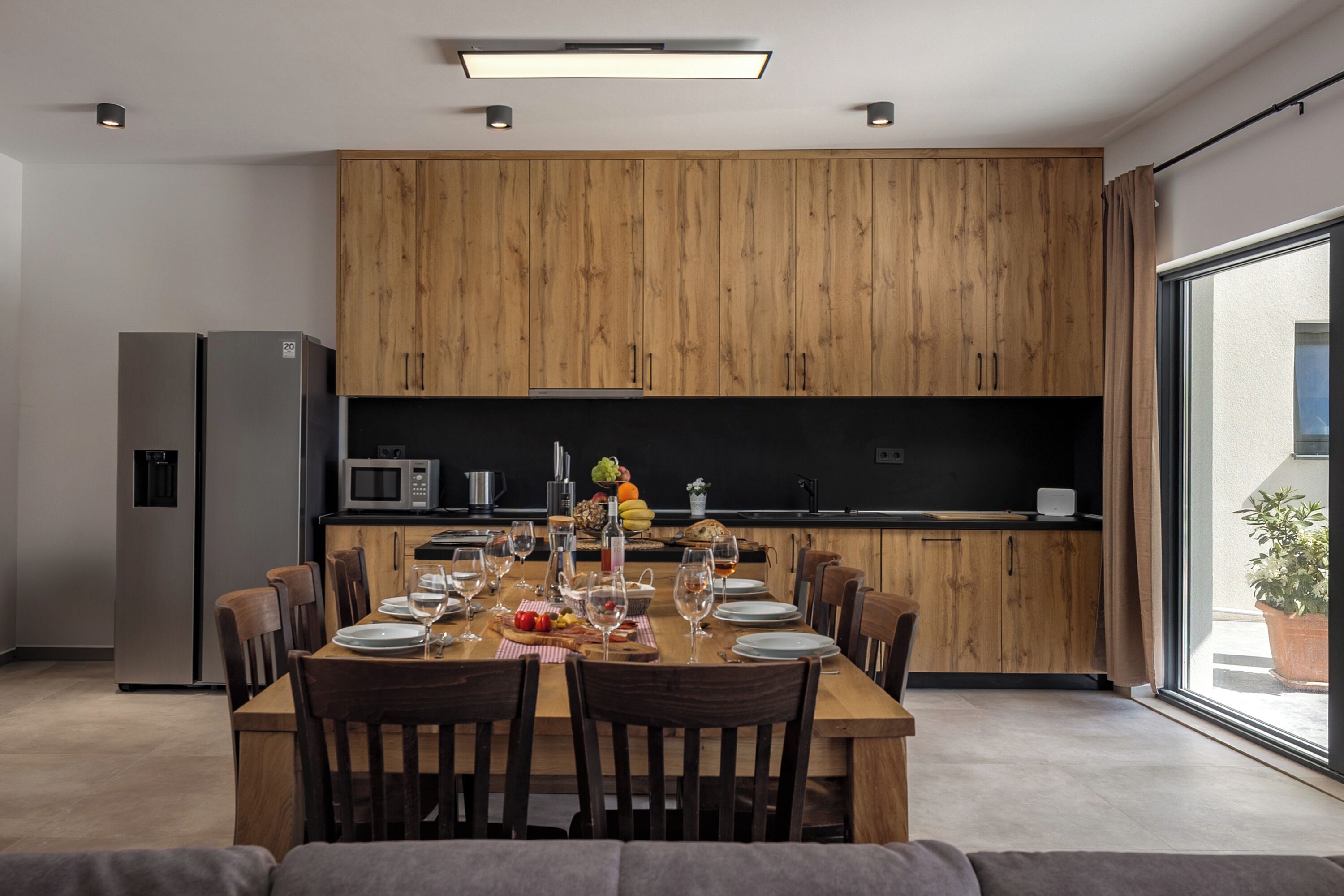 A modern kitchen with wooden cabinets, a dining table set for six, and a large window providing a view of the outdoors.