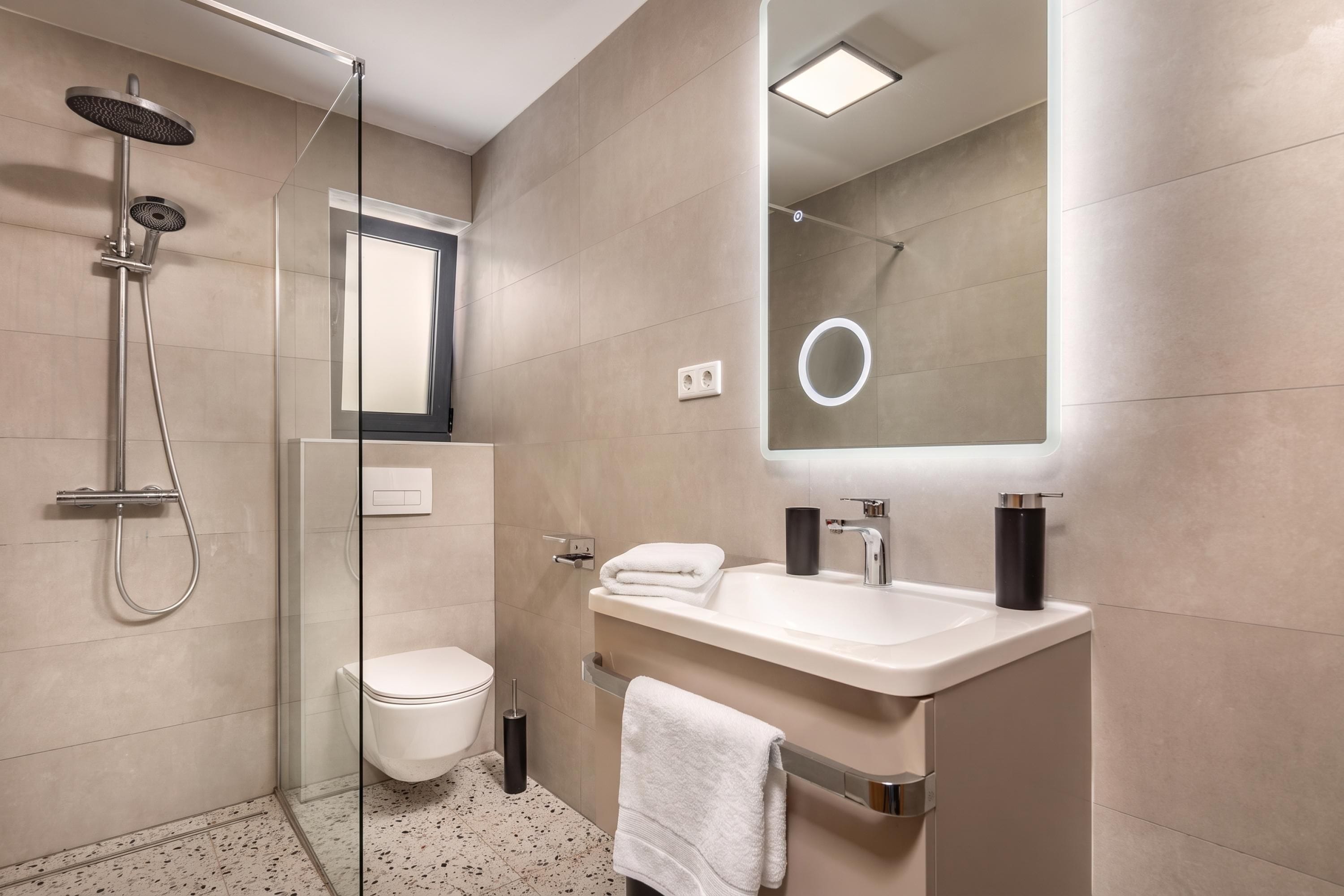 A modern bathroom with a glass-enclosed shower, a toilet, a sink with a mirror, and a towel rack.