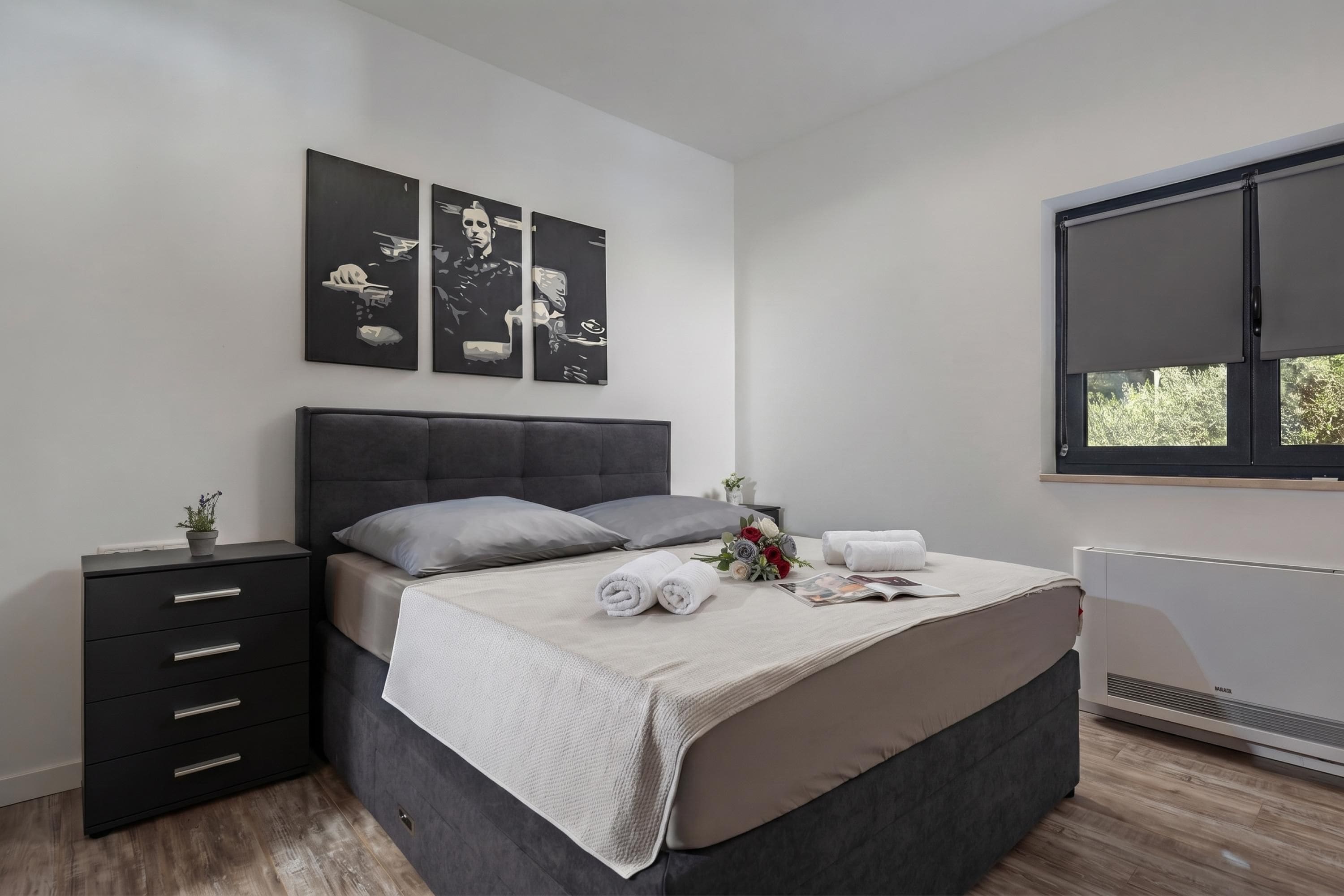 A modern bedroom with a bed, bedside tables, a radiator, and artwork on the wall.