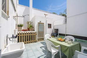 Un pequeño patio al aire libre con una mesa preparada para dos personas, un lavamanos y plantas en macetas.