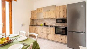 A modern kitchen with wooden cabinets, a stainless steel refrigerator, a microwave, and a gas stove. - Casa Torre San Giovanni 2-bed Apt Near Beach (Ugento)