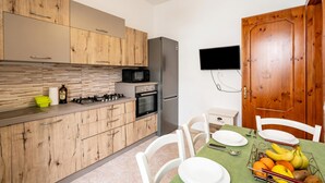 A modern kitchen with wooden cabinets, a stainless steel refrigerator, a microwave, and a dining area with a table set for two. - Casa Torre San Giovanni 2-bed Apt Near Beach (Ugento)