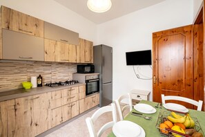 Una cocina moderna con armarios de madera, un refrigerador de acero inoxidable, un microondas y un comedor con una mesa dispuesta para dos personas.