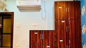 A room with a large wooden wardrobe, an air conditioning unit, and a fan. - Deena Residency (Varanasi)