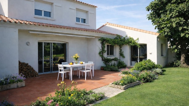 Ein weißes Haus mit Terrasse, Esstisch und Garten.