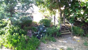 Ein Garten mit einem gepflasterten Weg, der zu einer Holztreppe führt, umgeben von üppigem Grün und einer Steinmauer.