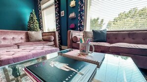 Un salon chaleureux aux murs de couleur turquoise, avec deux canapés roses, une table basse en verre sur laquelle sont posés des livres et une tasse, et un sapin de Noël.