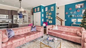 Un salon moderne avec des canapés roses, une table basse en verre et un mur d’accent de couleur turquoise orné de photos encadrées.