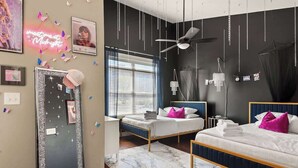 Une chambre avec deux lits, un ventilateur de plafond, un grand miroir et un panneau lumineux au néon.
